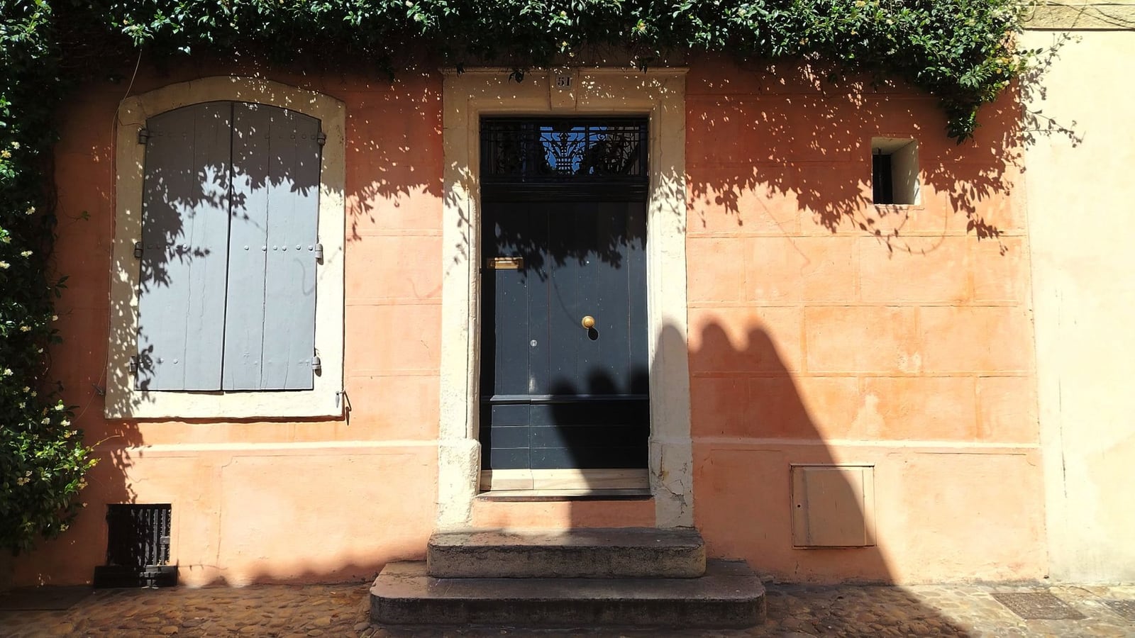 Façade provençale ocre rose avec porte d'entrée ancienne et volets sous le jasmin