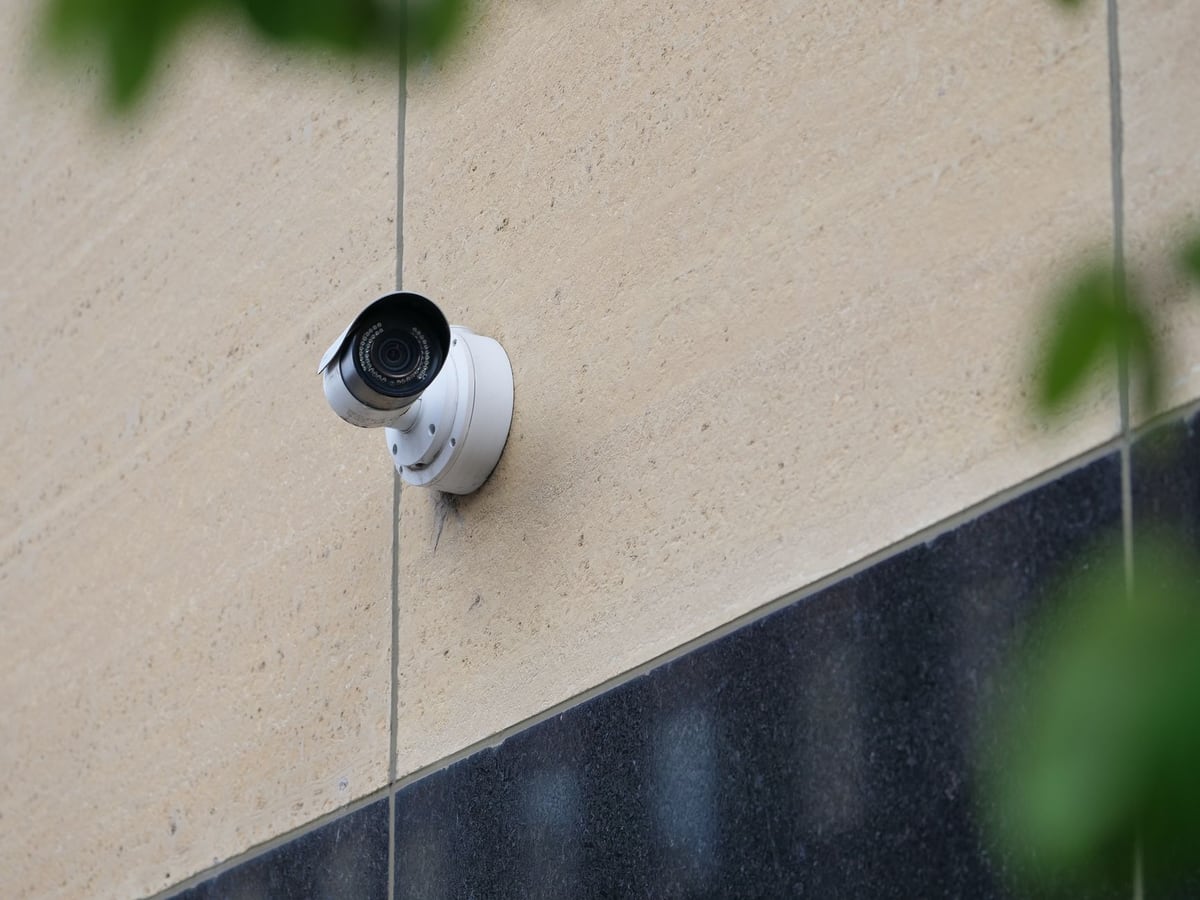 Caméra de surveillance blanche fixée sur le mur en pierre claire d'une maison