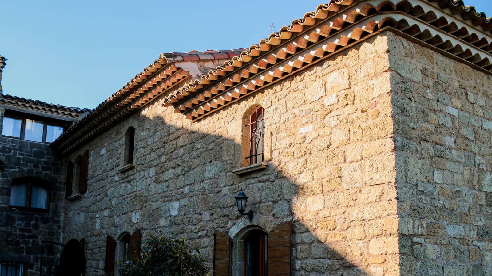 Maison en pierre du Sud avec génoise en tuiles et lanterne murale sous la lumière dorée
